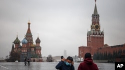 FILE - A man puts on a protective face mask as he stands with another person in a deserted Red Square in Moscow, Russia, Oct. 28, 2021.