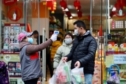 A worker measures the body temperature of people leaving a supermarket in Qingshan district following an outbreak of the novel coronavirus in Wuhan, Hubei province, China, Feb. 7, 2020.