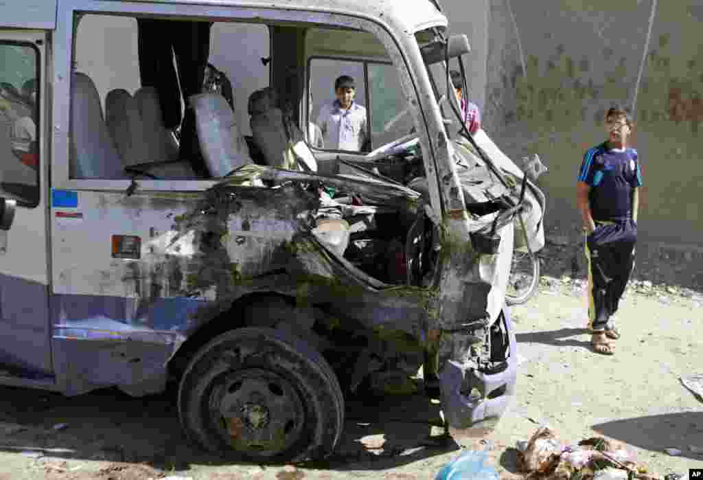 2013年3月19日，巴格达市什叶派重镇萨德尔城发生一起汽车炸弹袭击事件后，孩子们查看一辆被摧毁的巴士。