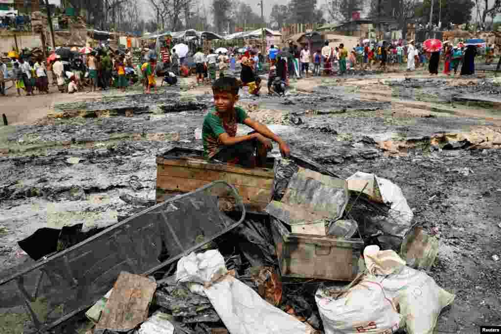 A Rohingya refugee boy sits on a stack of burned material after a massive fire broke out and destroyed thousands of shelters at a Rohingya refugee camp in Cox&#39;s Bazar, Bangladesh.