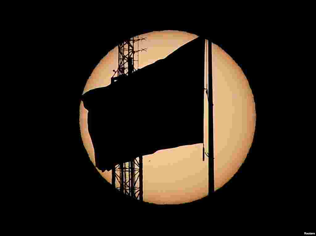 Một lá cờ Mỹ in bóng đen trong khi Sao Thủy được nhìn thấy ở góc phần tư bên trái phía dưới di chuyển ngang qua bề mặt mặt trời ở thành phố Las Vegas, bang Nevada, Mỹ.