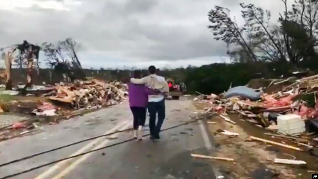Warga berjalan di antara puing-puing yang berserakan pasca dihantam tornado di Lee County, Alabama, Minggu, 3 Maret 2019.
