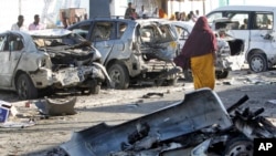 Somalíes caminan frente a vehículos dañados por el ataque a un restaurante en Mogadishu, Somalia, el viernes, 22 de enero de 2016.
