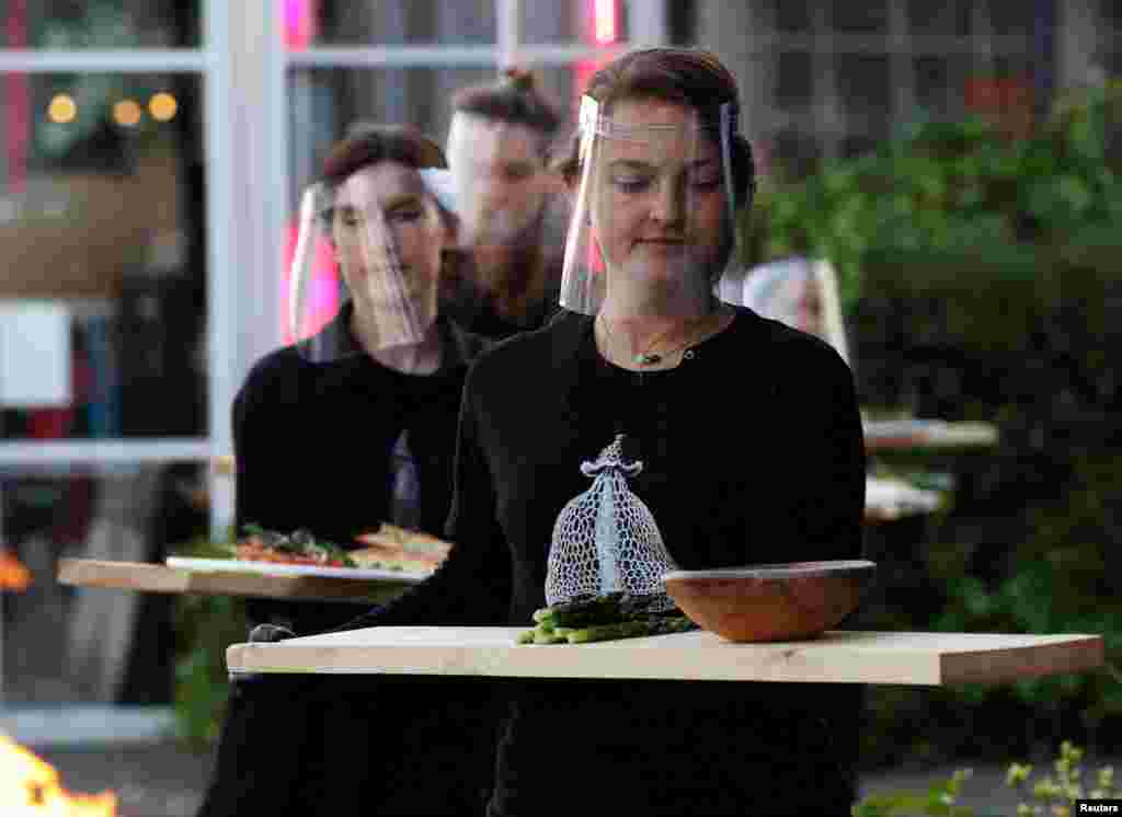 Servers in protective gear carry food at a restaurant which is testing servers providing drinks and food to models pretending to be clients in a safe &quot;quarantine greenhouses&quot; in Amsterdam, Netherlands, May 5, 2020.