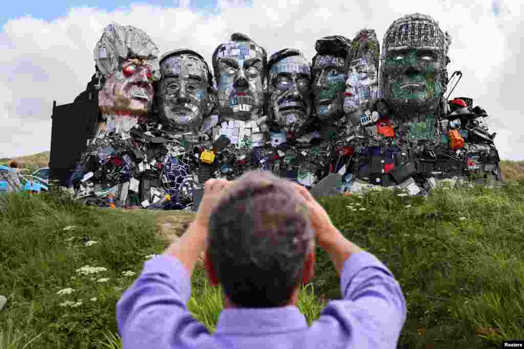A man photographs &quot;Mount Recyclemore,&quot; an artwork depicting the G-7 leaders looking toward Carbis Bay, made from electronic waste by Joe Rush and Alex Wreckage, ahead of the G-7 summit, at Hayle Towans in Cornwall, Britain.