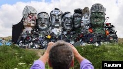 A man photographs &quot;Mount Recyclemore,&quot; an artwork depicting the G-7 leaders looking toward Carbis Bay, made from electronic waste by Joe Rush and Alex Wreckage, ahead of the G-7 summit, at Hayle Towans in Cornwall, Britain.