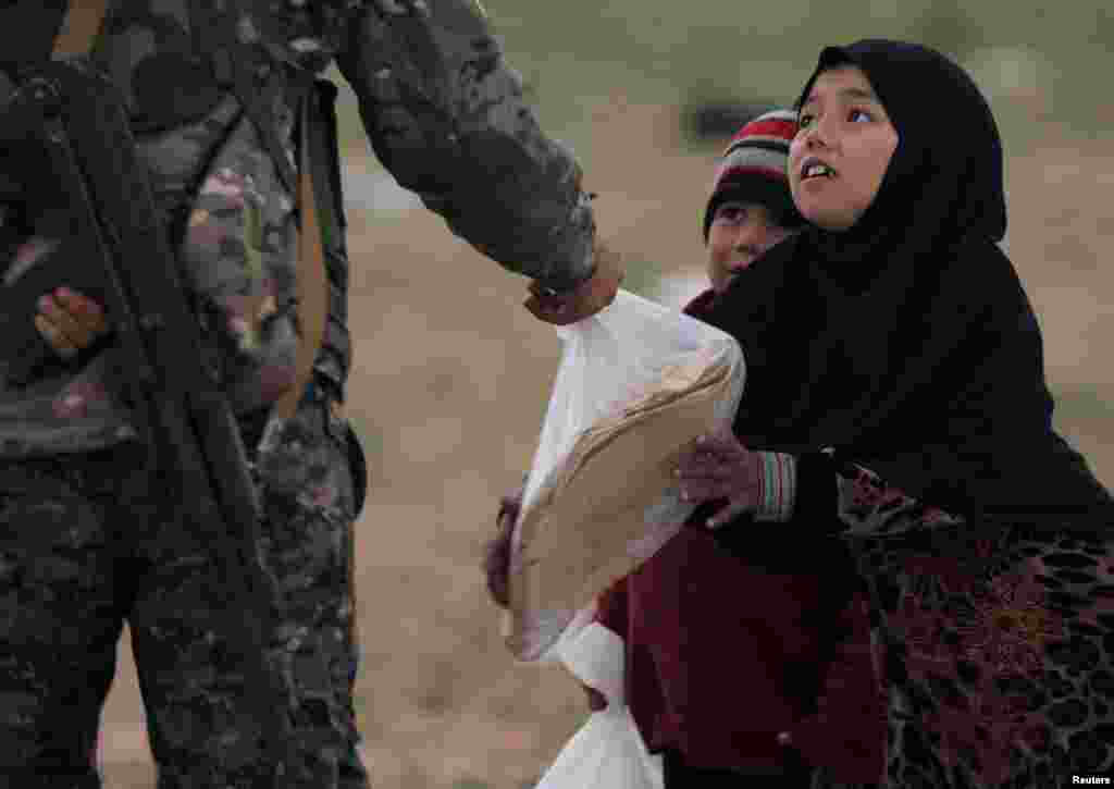 A girl takes a stack of bread from a fighter of Syrian Democratic Forces (SDF) near the village of Baghouz, Deir Al Zor province, Syria, Feb. 27, 2019.