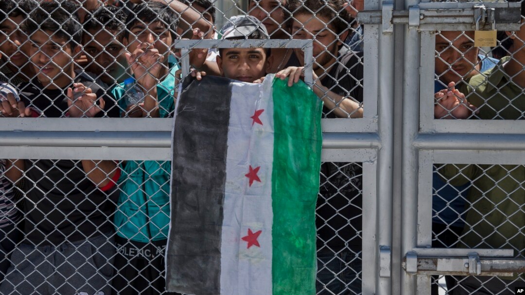 Para migran dan pengungsi berdiri dibalik pintu besi yang terkunci saat kunjungan Paus Fransiskus ke pusat penahanan pengungsi Moria di Pulau Lesbos, Yunani, 16 April 2016. (Foto: AP)