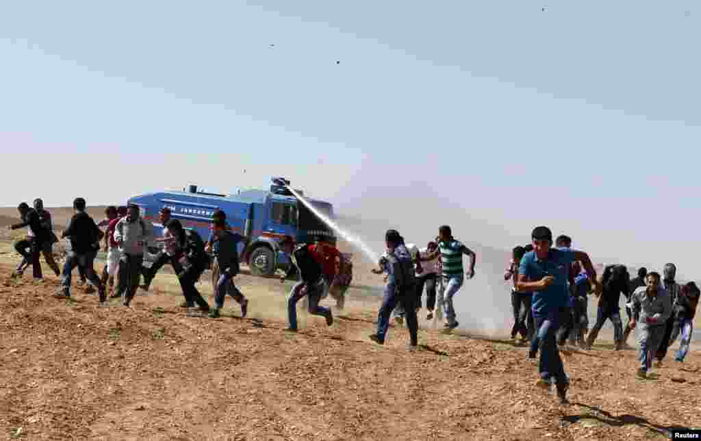 Protesters run away as an armoured army vehicle sprays water to disperse them during a pro-Kurdish demonstration in solidarity with people of Kobani, near the Mursitpinar border crossing on the Turkish-Syrian border, in the Turkish town of Suruc in southe