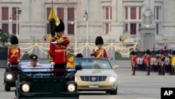 Thailand's King Maha Vajiralongkorn, standing in a car right, and Queen Suthida, standing in a car left, review the honor guard in Bangkok, Thailand, Dec. 3, 2024.