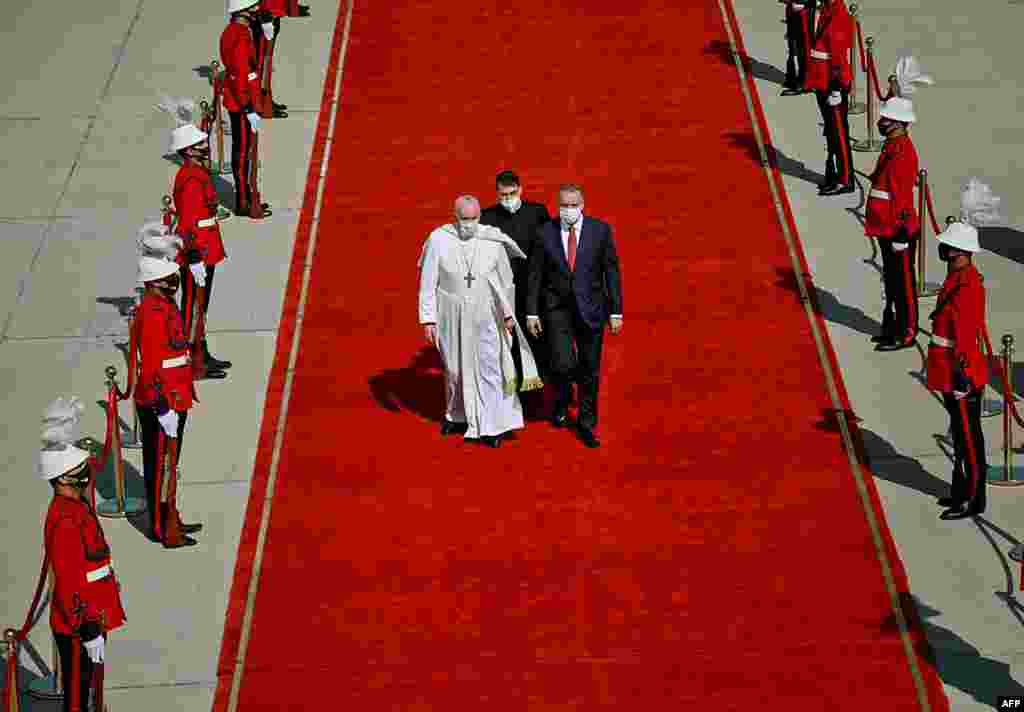Prime Minister Mustafa al-Kadhemi escorts Pope Francis upon his arrival at Baghdad International Airport to start the first-ever papal visit to the country, in this handout image released by the press office of Iraqi Prime Minister on its Facebook page. 