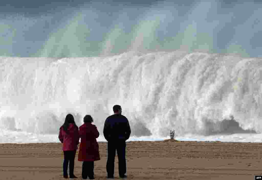 Flowers are seen on the sands of a beach in Meco, near Sesimbra as people watch the waves after one university student died and five others are missing when the group of seven were swept away by a huge wave on a beach in Portugal on Dec. 15.