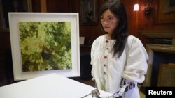 Robot artist 'Ai-Da' sketches using a pencil attached to her robotic arm, while standing next to a painting based on her computer vision data when run through algorithms developed by computer scientists in Oxford, Britain, June 4, 2019.