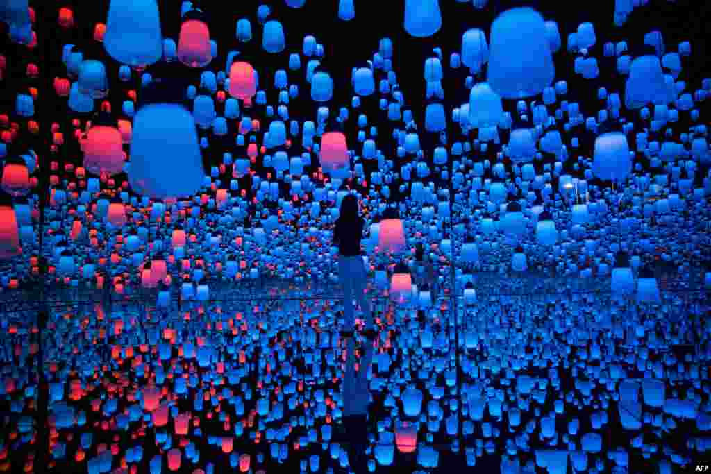 A member of Teamlab collective walks in a digital installation room with hanging lamps at Mori Building Digital Art Museum in Tokyo, Japan.