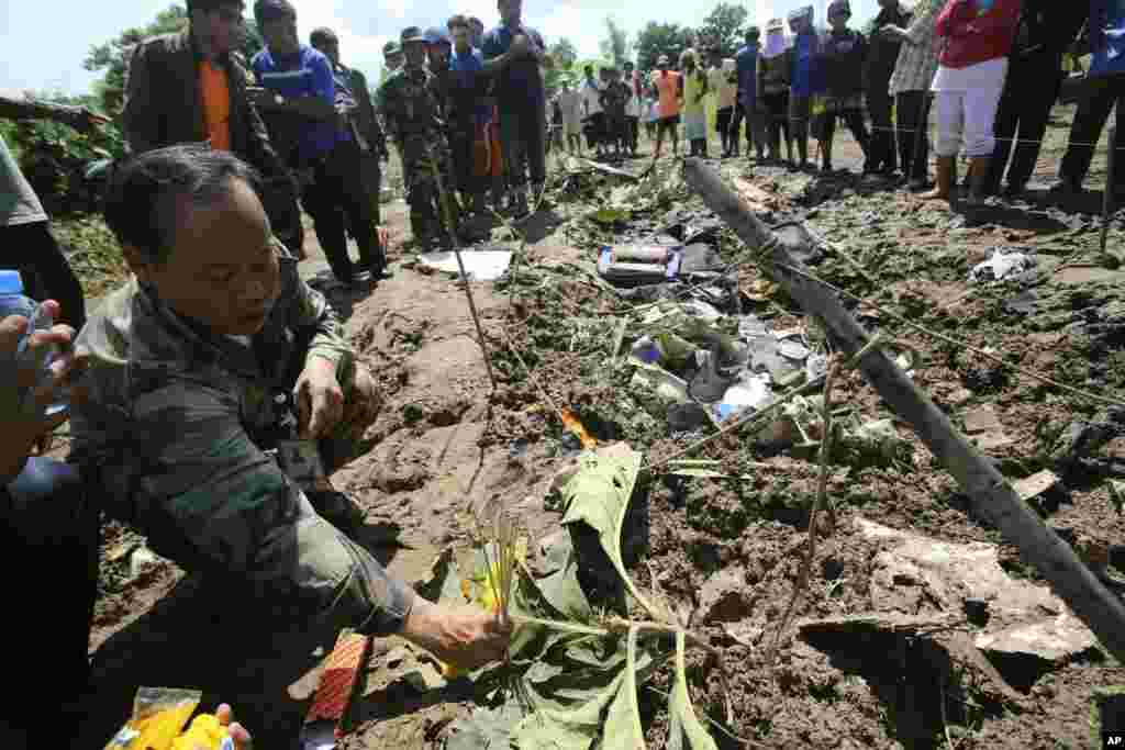 A Lao soldier places incense sticks into the ground beside the wreckage left by a Lao Airlines turboprop plane as he pays his respects to the victims of the ill-fated flight, in Pakse, Laos, Oct. 17, 2013.