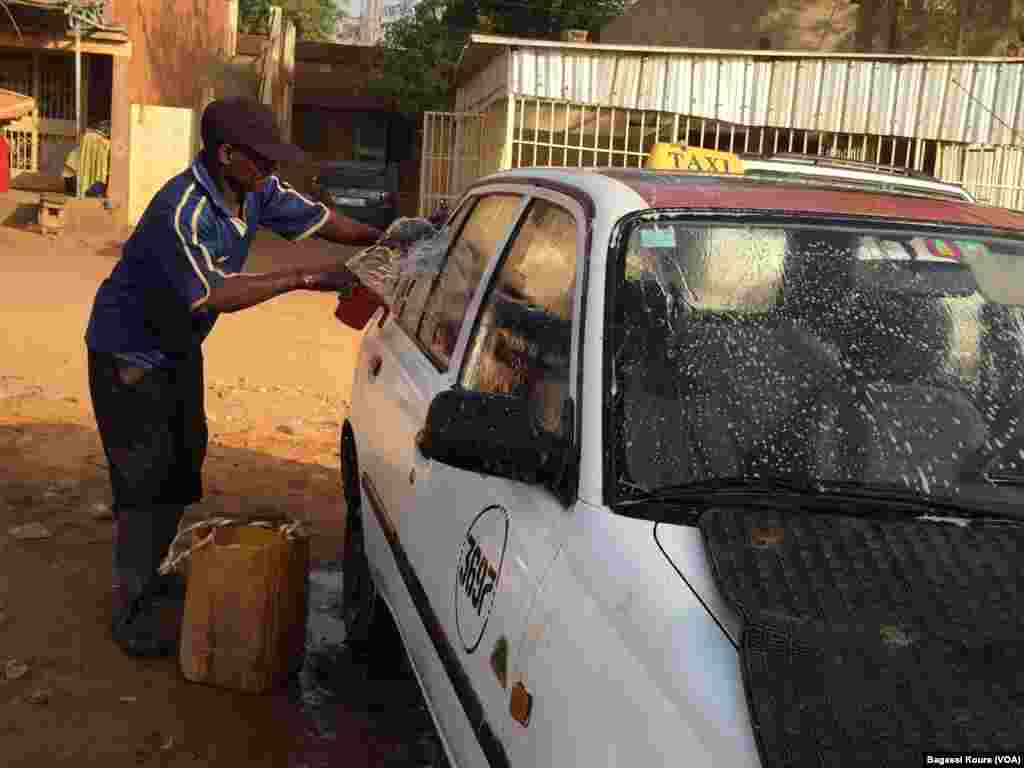 Un chauffeur de taxi lave son véhicule dans une rue de Niamey, le 16 mars, 2016. (VOA/Bagassi Koura)