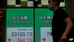 A man wearing a face mask walks past a bank's electronic board showing the Hong Kong share index at Hong Kong Stock Exchange Monday, March 30, 2020.