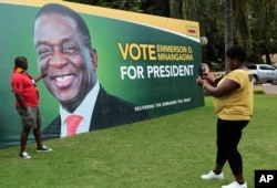FILE - A man has his picture taken in front of an election campaign poster of Zimbabwe President Emmerson Mnangagwa portrait, in Harare, May, 4, 2018.