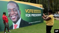 FILE - A man has his picture taken in front of an election campaign poster of Zimbabwe President Emmerson Mnangagwa portrait, in Harare, May, 4, 2018.