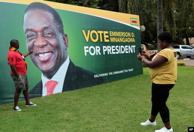 FILE - A man has his picture taken in front of an election campaign poster of Zimbabwe President Emmerson Mnangagwa portrait, in Harare, May, 4, 2018.