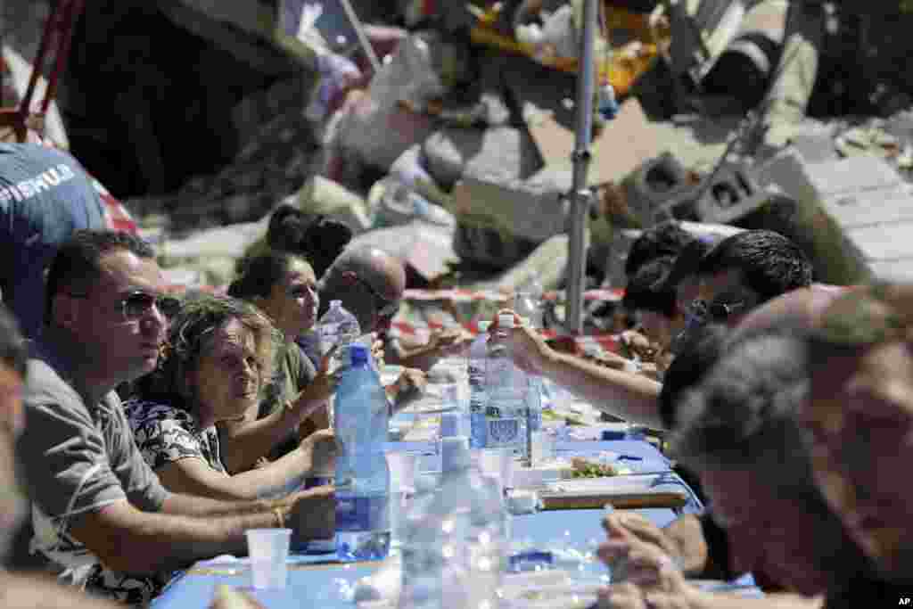Homeless, volunteers and rescuers eat their lunch in a camp outside the severely damaged town of Illica, central Italy, Aug. 25, 2016.
