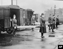In this October 1918 photo made available by the Library of Congress, St. Louis Red Cross Motor Corps personnel wear masks as they hold stretchers next to ambulances in preparation for victims of the influenza epidemic.
