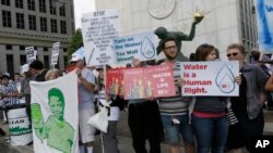 FILE - People stand outside Detroit City Hall, protesting thousands of residential water-service shutoffs by Detroit's water department, during a rally in Detroit, Thursday, July 24, 2014.