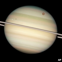 FILE - This image provided by NASA captures the transit of several moons across the face of Saturn. The giant orange moon Titan – larger than the planet Mercury – can be seen at upper right.