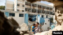 Palestinian man carries boy past UN-run school that was struck whole sheltering those displaced by Israeli ground offensive, Jebalya northern Gaza, July 30, 2014.