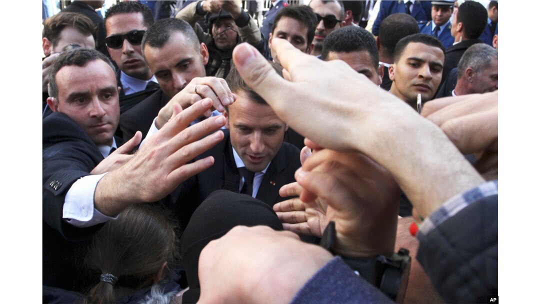 French President Emmanuel Macron is protected by security members as he meets residents in Algiers, Wednesday, Dec.6, 2017. Macron is traveling to Algeria for a one-day working visit aimed at boosting the security and economic cooperation between the two countries.