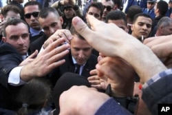 French President Emmanuel Macron is protected by security members as he meets residents in Algiers, Wednesday, Dec.6, 2017. Macron is traveling to Algeria for a one-day working visit aimed at boosting the security and economic cooperation between the two countries.