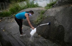 Una mujer que usa una máscara facial como medida de precaución en medio de la propagación del COVID-19 recoge agua de la ladera de una montaña en Caracas.