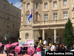 The Cuban flag flies over country's Embassy in Washington D.C. as people holding posters shout slogans, a few minutes after re-opening ceremony, July 20, 2015. (VOA/ P. Dockins)