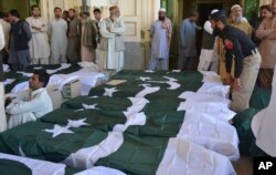 FILE - People wait to carry the bodies of their family members who died in an attack on the Police Training Academy, in Quetta, Pakistan, Oct. 25, 2016.