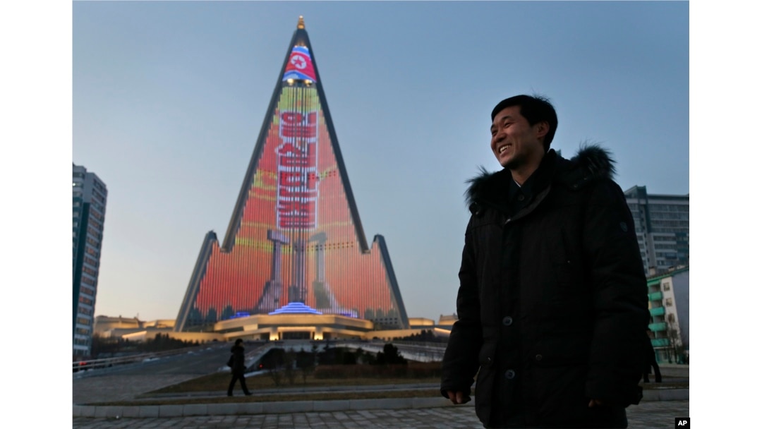 Light designer Kim Yong Il smiles, Dec. 20, 2018, as his light show on the facade of the Ryugyong Hotel is seen in the background. For several hours each night, the building that doesn't have electricity inside becomes the backdrop of a massive light show in which more than 100,000 LEDs flash images of famous statues and monuments, bursts of fireworks, party symbols and political slogans.