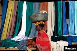 FILE - A woman carries a bucket on her head as she walks past fabrics for sale in Gao, Mali, Feb. 2013.