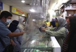 Petugas toko melayani pelanggan dari balik selembar plastik yang dipasang untuk membantu mengekang penyebaran virus corona di sebuah apotek di Jakarta, Senin, 6 April 2020. (AP)