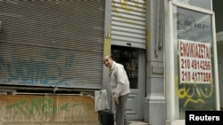 A man prepares to leave his shop next to an empty one with a sign reading "For Rent" in Piraeus port-town near Athens, May 29, 2012. 