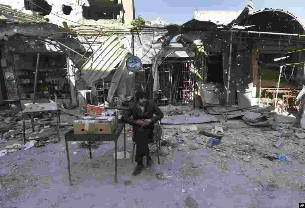 2013年2月26日一個擺地攤買香煙的小販坐在敘利亞伊德利卜省的邁阿拉努阿曼的被炮擊毀壞的店鋪前面。