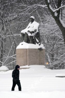 Un hombre solitario camina en una ligera tormenta de nieve a través del Grant Park de Chicago el domingo 31 de enero de 2021, pasando por una estatua nevada de Abraham Lincoln.