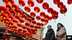 Women wearing face masks to help curb the spread of the coronavirus walk under red lanterns hanging along an alley near the Houhai Lake in celebration of the Lunar New Year in Beijing, Thursday, Feb. 11, 2021.