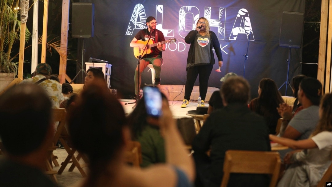 In this Jan. 12, 2019 photo, Venezuelan singer Reymar Perdomo performs with fellow Venezuelan and guitarist Omar Rumbos at a fair on the beach of San Bartolo, Peru. 