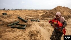 Seorang warga Palestina menggendong bayi berjalan melewati kontainer amunisi yang ditinggalkan oleh pasukan Israel saat dia melarikan diri lebih jauh ke selatan dari Khan Yunis di Jalur Gaza selatan, 2 Februari 2024. (Mahmud Hams / AFP)