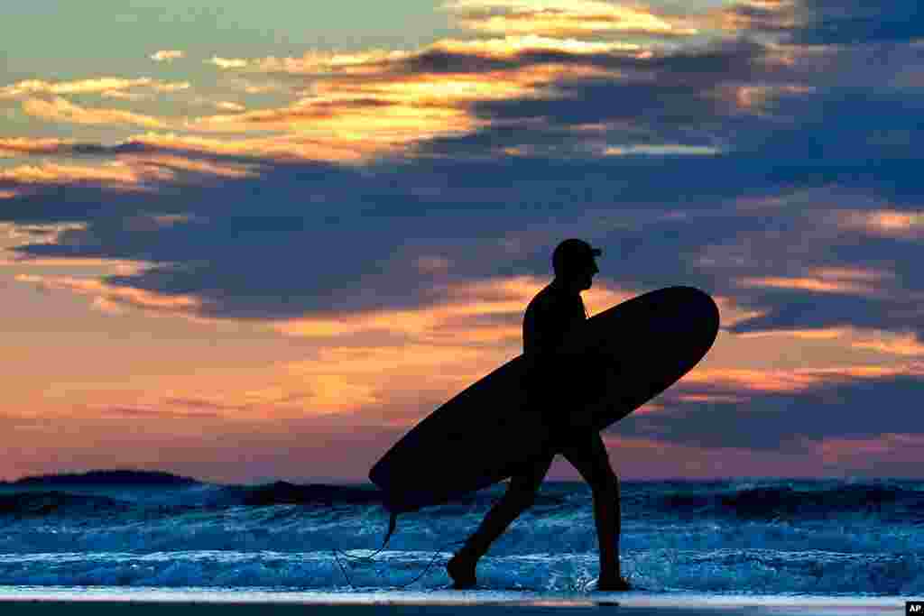 A surfer heads out to ride the waves on another unusually mild morning at Old Orchard Beach, Maine.