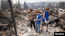From left, Mim Morris looks through the remnants of her home, which was destroyed by the Carlton Complex Fire, as her grandsons Sean Lafer, 12, and Joel Lafer, 14, join her near Malott, Washington, July 20, 2014.