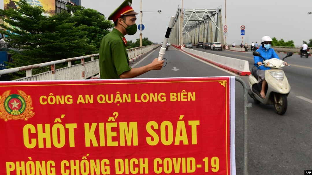 Một công an đứng canh tại một chốt kiểm soát ở Hà Nội ngày 29/7/2021. Bộ Y tế Việt Nam vừa quyết định giảm thời gian cách ly tập trung cho người nhập cảnh đã tiêm vaccine đầy đủ xuống còn 7 ngày.