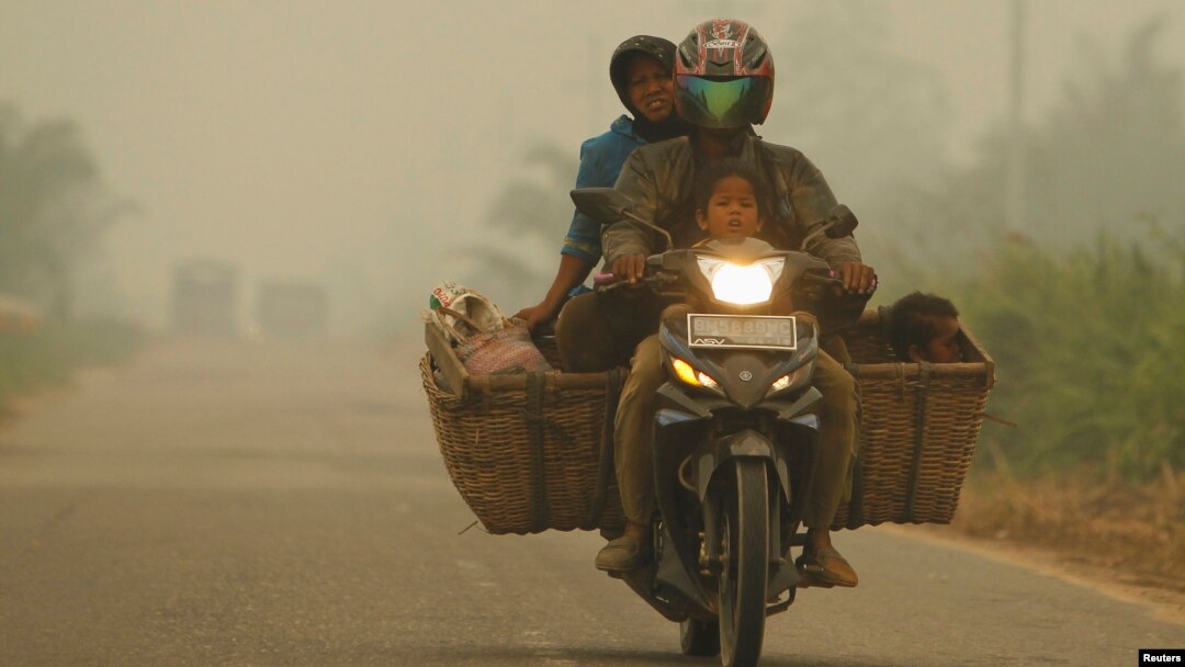 A family rides on a motorcycle as the haze from fires hits Kubu district in Rokan Hilir, in Indonesia's Riau province, June 25, 2013.