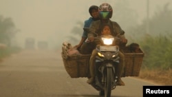 A family rides on a motorcycle as the haze from fires hits Kubu district in Rokan Hilir, in Indonesia's Riau province, June 25, 2013.