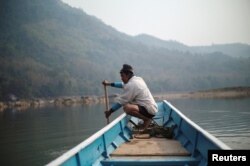 FILE - A local villager drives a boat where the future site of the Luang Prabang dam will be on the Mekong River, on the outskirts of Luang Prabang province, Laos, Feb. 5, 2020.