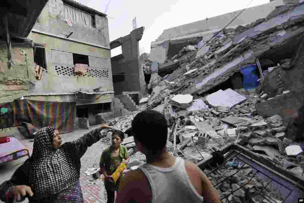 Heygar Jendiyah, left, points to where the family house kitchen once stood, partially destroyed by a previous air strike, as her children Ranin, 10, center, and Helmi, right, listen, in the Sabra neighborhood of Gaza City, northern Gaza Strip,